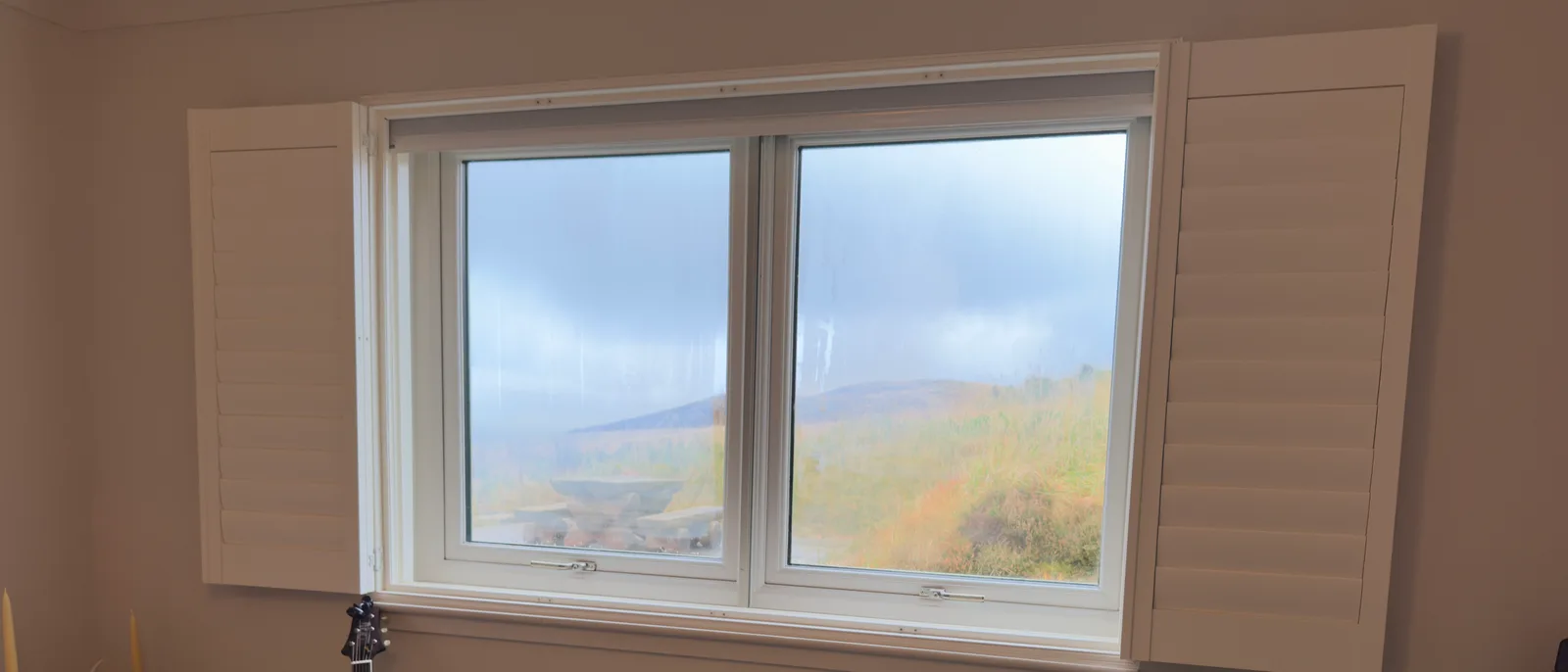 The same Shutter and Shade window with the cellular blind fully raised, leaving a clear window and the louvred shutters open to a Highland view