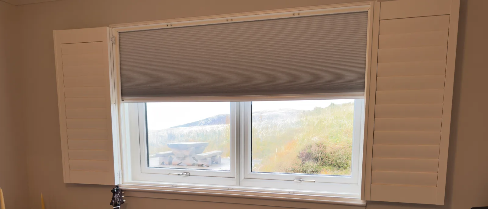 Room darkening Shutter and Shade: louvred interior shutters open on both sides with a cellular dim-out blind lowered over the top of the window, in a Highland room