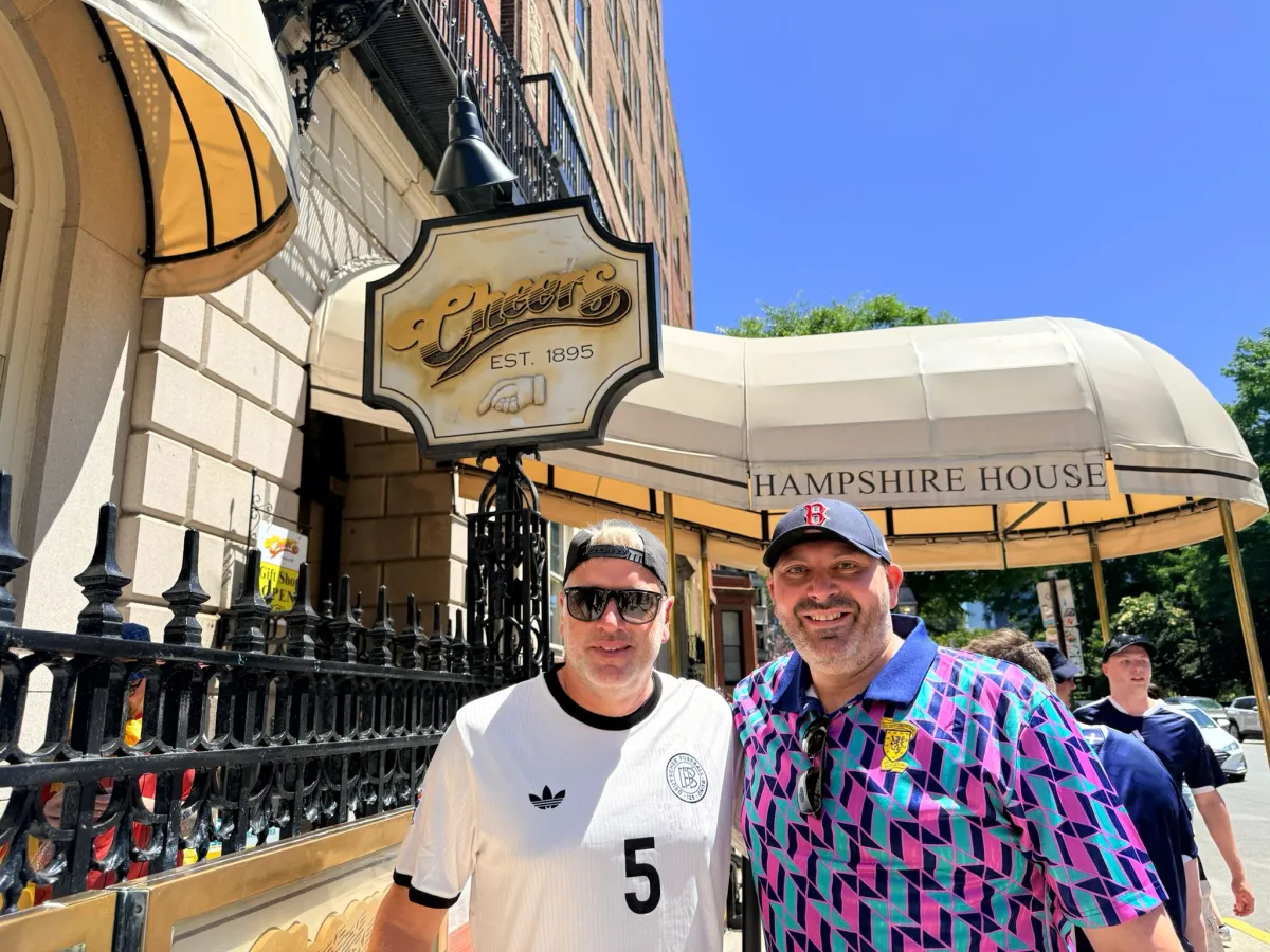 David D'Ambrosio in a Boston Red Sox cap and bright patterned top with his long standing friend Oliver Kupka in a white football shirt, outside the Cheers bar in Boston during the World Cup