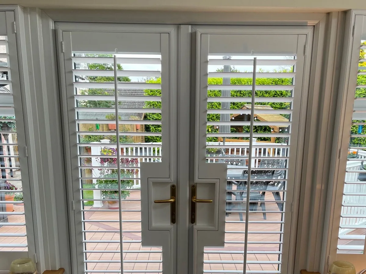 Full height shutters mounted directly to hinged patio doors with handle cut-outs revealing the brass door handles