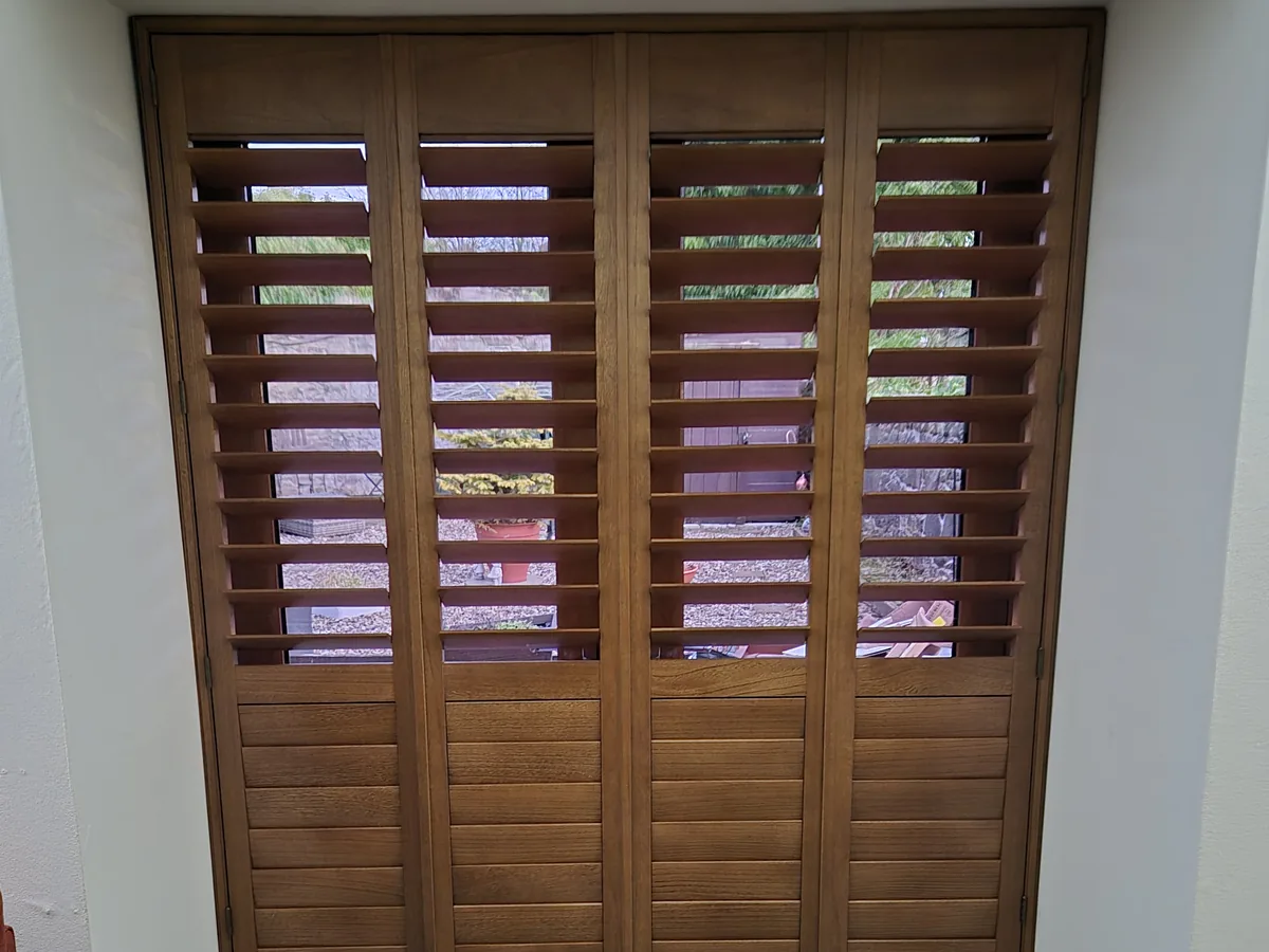 Brown wooden full height shutters with adjustable louvres covering patio doors in a modern interior
