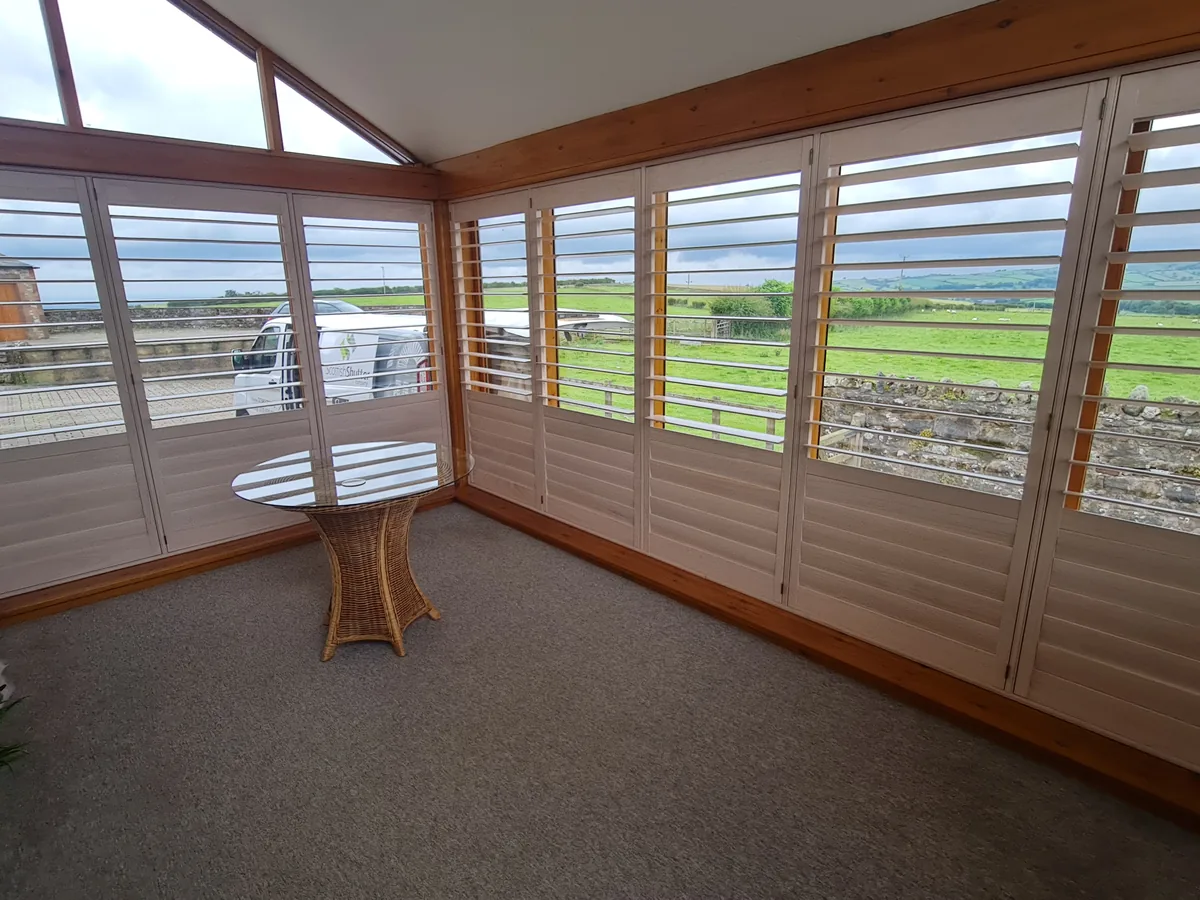 Full height shutters in a bright conservatory overlooking countryside
