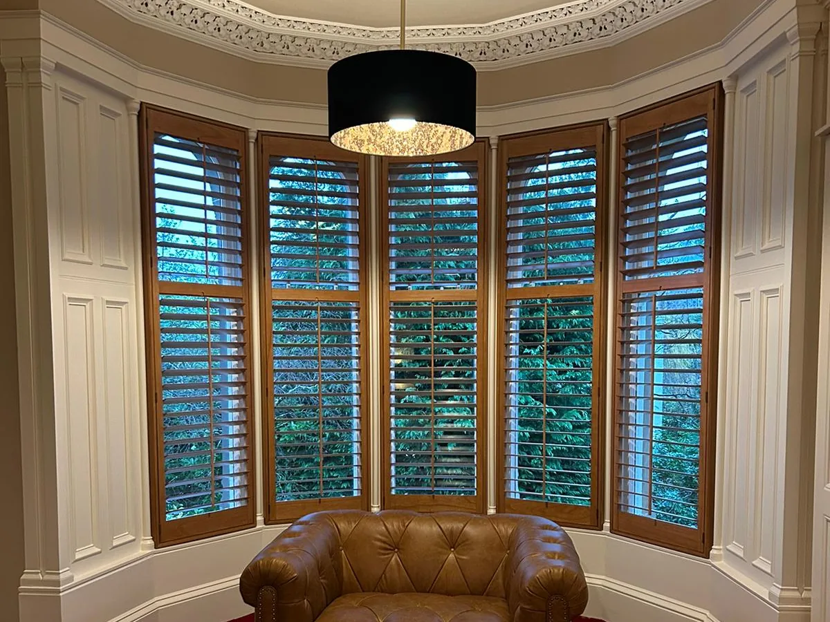 Wooden full height shutters fitted to a curved bow window in a Scottish bedroom